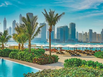 Städtische Poollandschaft mit Palmen, Sonnenschirmen und Hochhäusern im Hintergrund bei klarem Himmel.