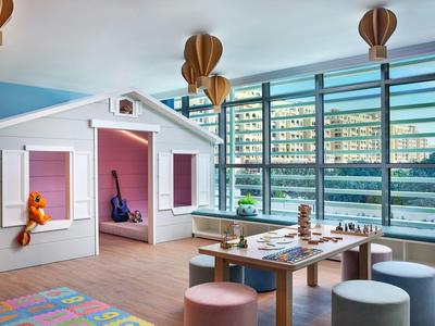 Kinderzimmer mit Spielhaus, buntem Teppich, rundem Tisch und großen Fenstern zum Flussufer.