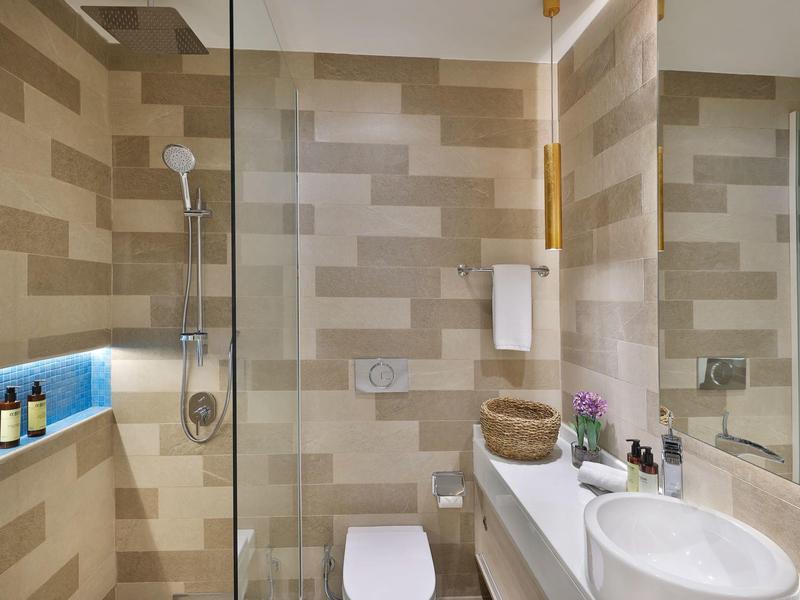 Modernes Badezimmer mit beigen Fliesen, Glasdusche, weißem WC und Waschbecken, Spiegel und Ablageflächen.