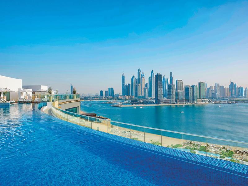 Infinity-Pool mit Blick auf eine Stadt mit modernen Hochhäusern am Meer unter blauem Himmel.