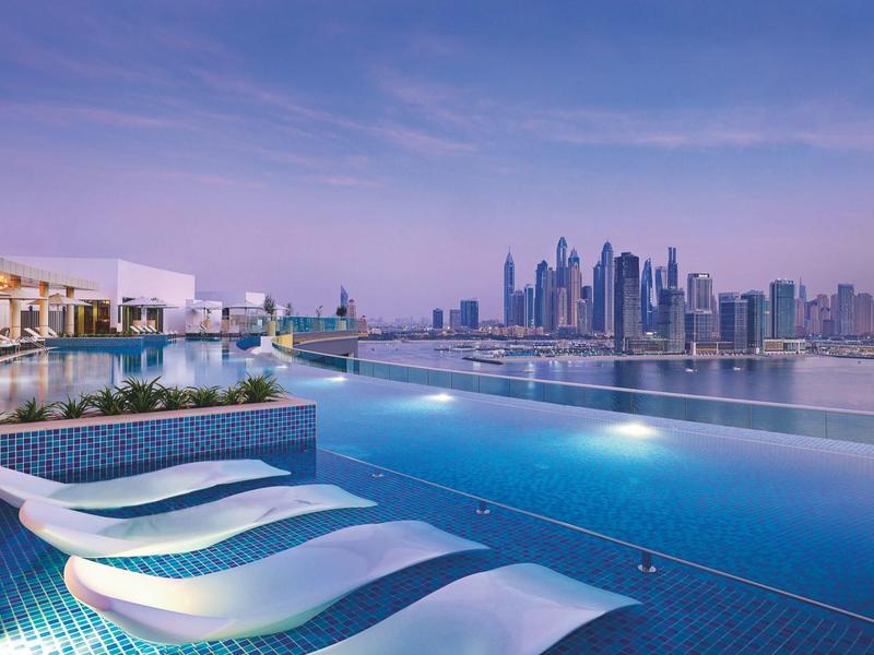 Infinity-Pool mit weißen Liegen und Blick auf eine moderne Stadtsilhouette bei Abenddämmerung.