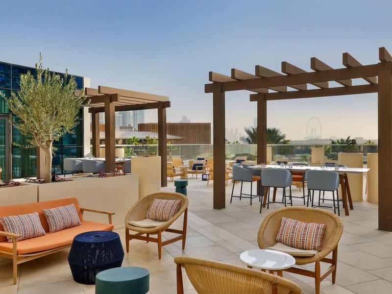 Moderne Dachterrasse mit Holzbalken, Sitzgruppen aus Korb und Sofa, Pflanze und klarer Himmel.