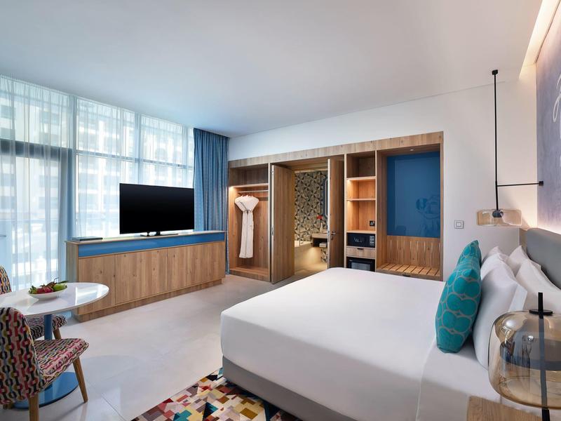 Modern eingerichtetes Schlafzimmer mit großem Bett, Holzschrank, Sessel und Fensterfront mit Vorhängen.