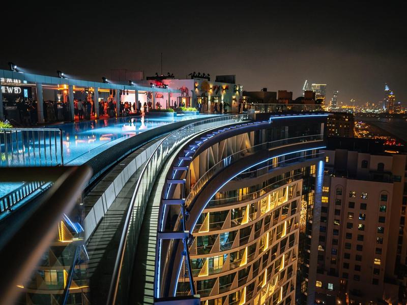 Moderne Hochhausfassade mit bunten Lichtern und glattem Geländer bei Nacht in der Stadt.