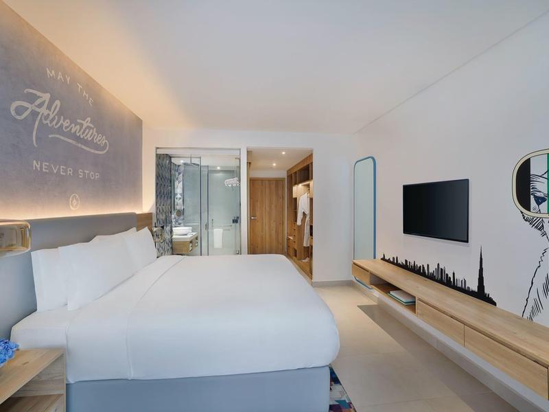 Modernes Hotelzimmer mit großem Bett, Glasbad, weißem Design und Wandgrafik im Raum.