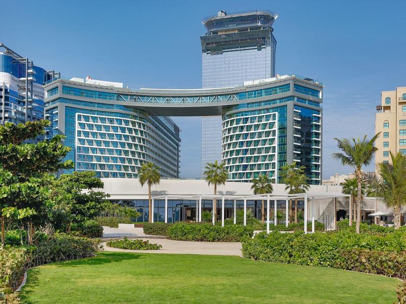 Modernes Hotelgebäude mit zwei geschwungenen Flügeln und gläsernem Verbindungssteg bei sonnigem Himmel.