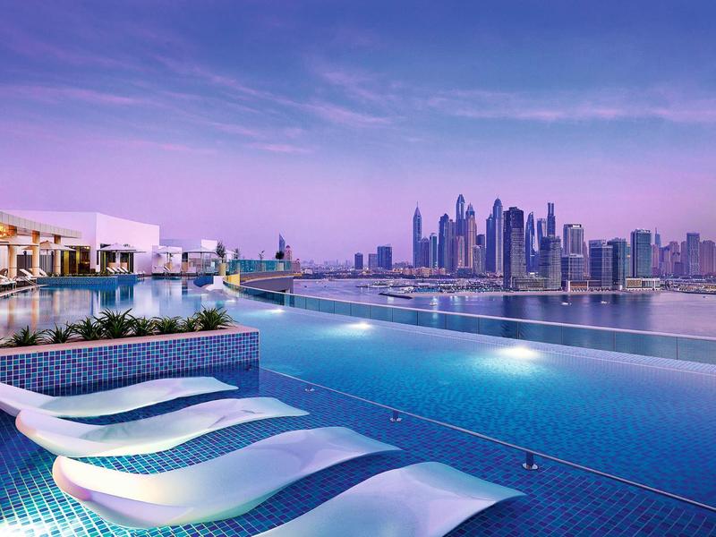 Infinity-Pool mit weißen Liegen und Blick auf moderne Hochhäuser in der Dämmerung.