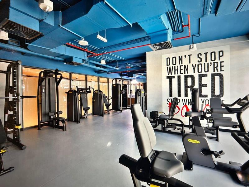 Moderner Fitnessraum mit blauer Decke, diversen Trainingsgeräten und motivierendem Wandzitat.