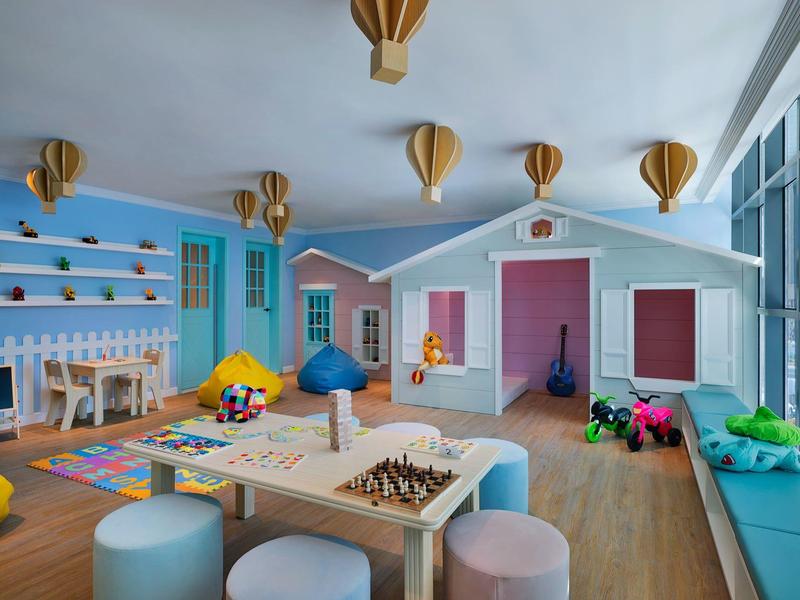 Buntes Kinderzimmer mit Rutsche, Spielzeug, Sitzkissen und Decken, helle Holzmöbel, große Fenster.