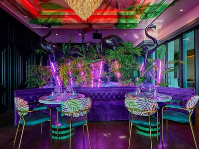 Bunte Bar mit lila Beleuchtung, grünen Pflanzen und stilvollen Stühlen in modernem Design.