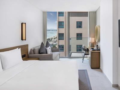 Modernes Hotelzimmer mit großem Bett, Sofa, Schreibtisch und Blick auf benachbartes Gebäude.