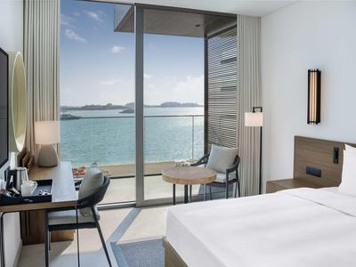 Modernes Hotelzimmer mit großem Bett, Schreibtisch und Meerblick durch bodentiefe Fenster.