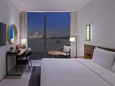 Modernes Hotelzimmer mit großem Bett, Schreibtisch, Stuhl, runder Spiegel und Blick auf Fluss bei Nacht.