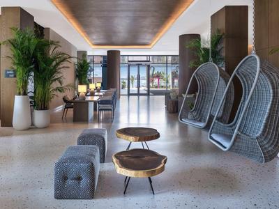 Moderner Innenraum mit grauen Hängesesseln, Holztischen, grauen Hockern und großen Pflanzen.