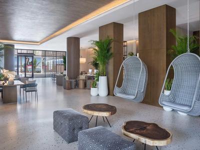 Nowoczesna lobby hotelowa z wiszącymi białymi wiklinowymi fotelami i drewnianymi akcentami wnętrza.