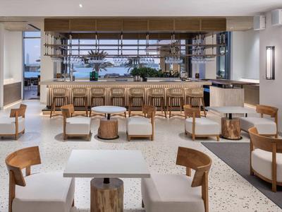 Moderner Kaffeehausraum mit Holzstühlen, weißen Polstern und großem Fenster mit Außenblick.