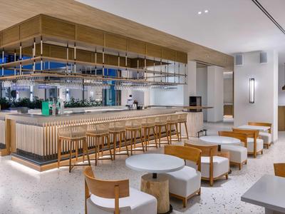 Nowoczesny bar hotelowy z drewnianym kontuarem, stołkami barowymi i przytulnymi miejscami do siedzenia w jasnym designie.