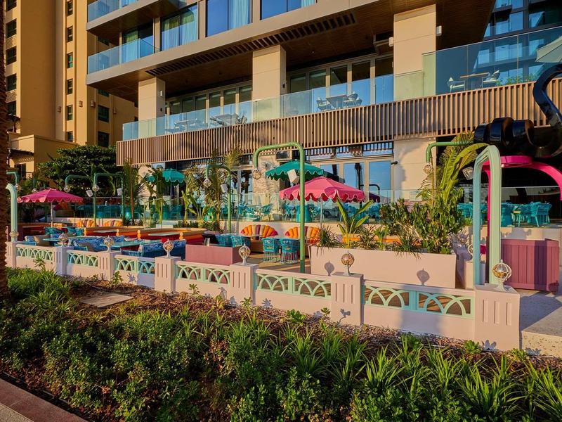 Bunte Kinderspielplatz mit Schaukeln, Rutschen und Flamingofiguren vor modernem Wohnhaus.