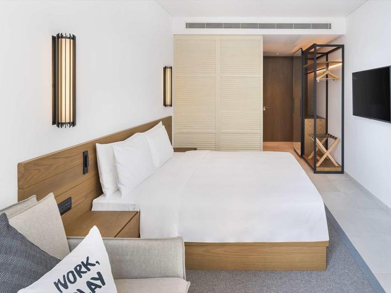 Modernes Hotelzimmer mit großem Bett, Holzrahmen, weißen Wänden und grauem Teppichboden.