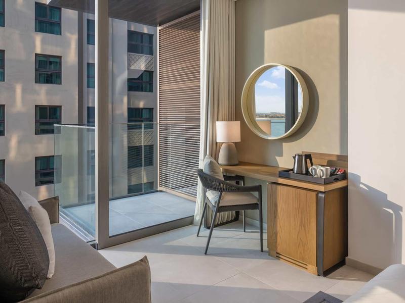 Moderner Raum mit Sofa, Schreibtisch, Stuhl, rundem Spiegel und großen Fenstern mit Stadtblick.
