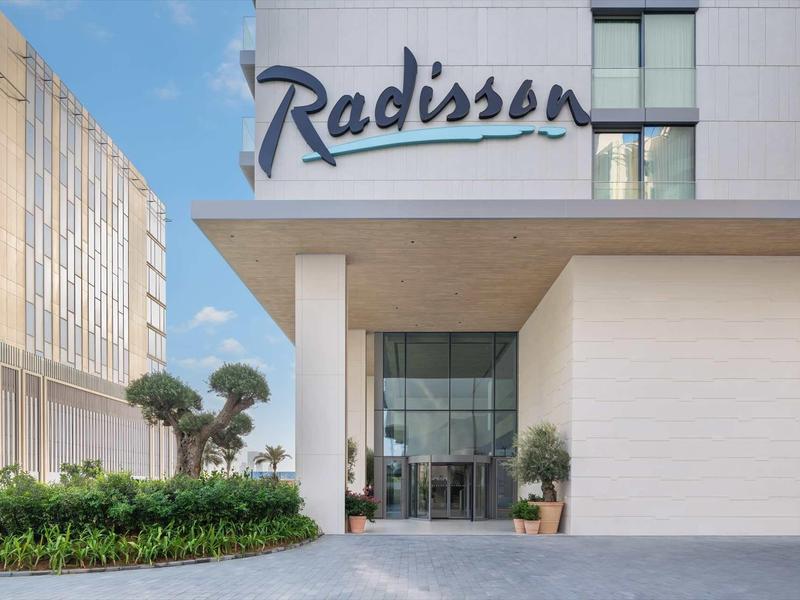 Eingang eines Radisson Hotels mit moderner Architektur, Glasfassade und grüner Bepflanzung.