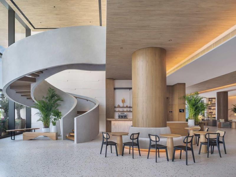 Moderner Innenraum mit spiralförmiger Treppe, Holzsäule, Tischen und Stühlen in hellem Ambiente.