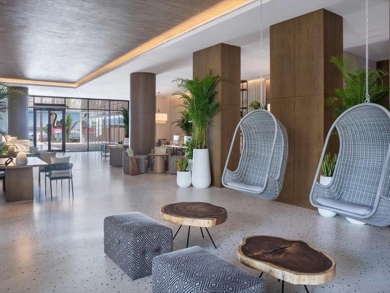 Moderner Lounge-Bereich mit hängenden Korbsesseln, kleinen Holztischen und großen Pflanzen in hellem Raum.