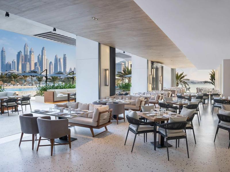 Moderner Außenbereich mit bequemen Sitzgruppen, runden Tischen und Blick auf die Skyline.