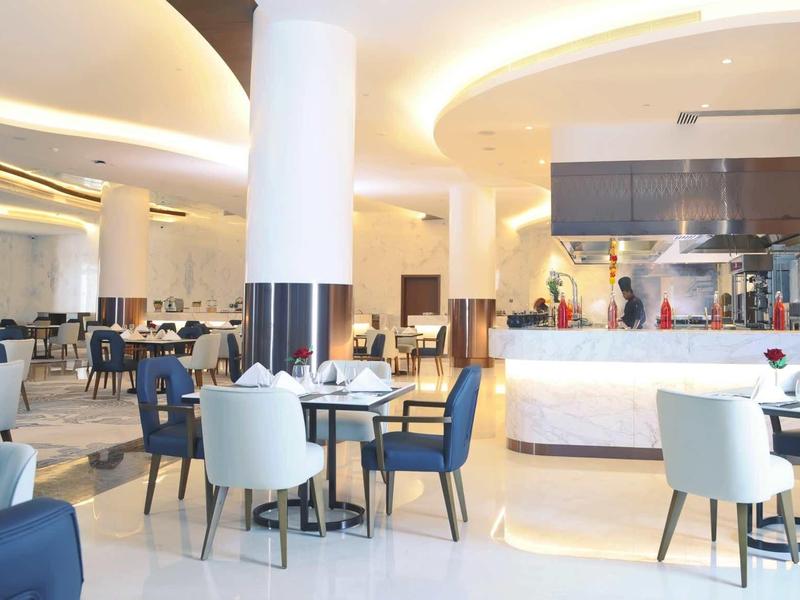 Innenraum eines modernen Restaurants mit hellen Stühlen, dunklen Tischen und großem Küchenbereich.