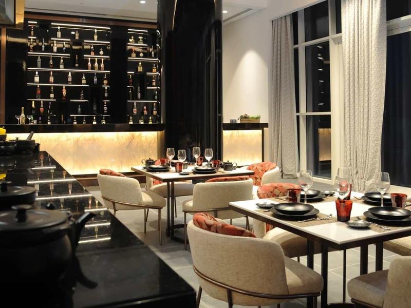 Modernes Café mit Holzboden, großen Fenstern, gemütlichen Sesseln und Tischen, warmes Licht.