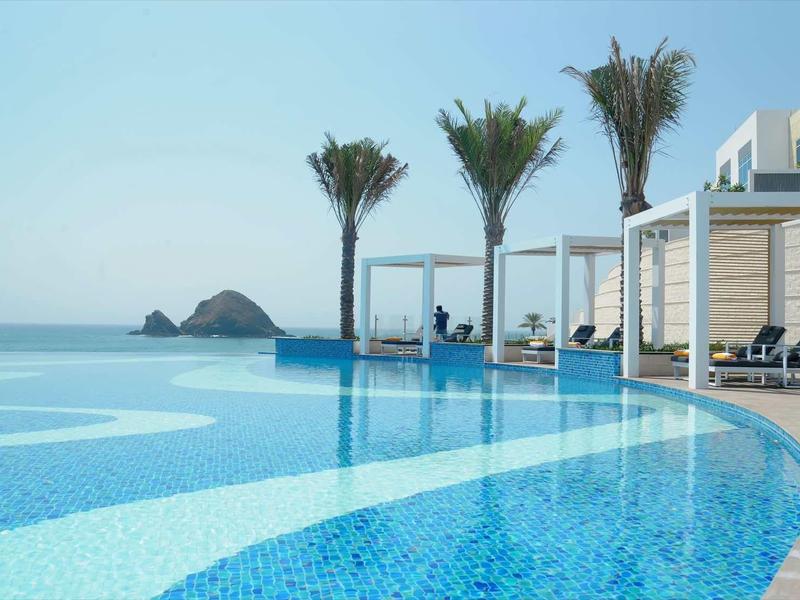 Infinity-Pool mit türkisblauem Wasser, Palmen und weißen Sonnenschirmen an der Küste.