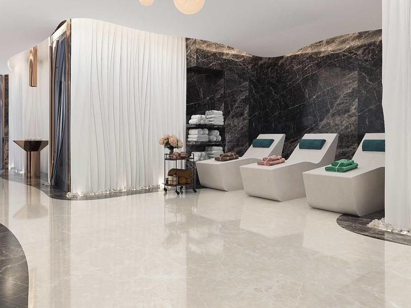 Moderner Wellnessbereich mit Liegestühlen, weißen Vorhängen und dunkler Marmorwand.