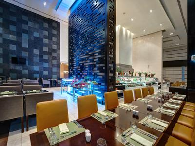 Elegantes Restaurant mit langen Holztischen, gelben Stühlen und moderner, dunkler Wandgestaltung.