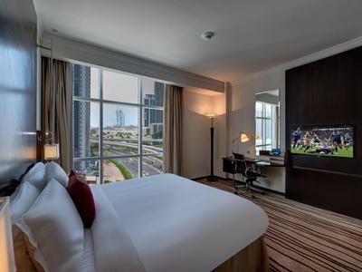 Modernes Hotelzimmer mit großem Bett, Schreibtisch, Flachbildschirm und Blick auf Stadtgebäude.