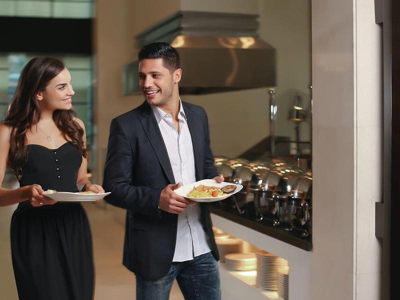 A couple carrying plates with food in an elegant hotel buffet area.