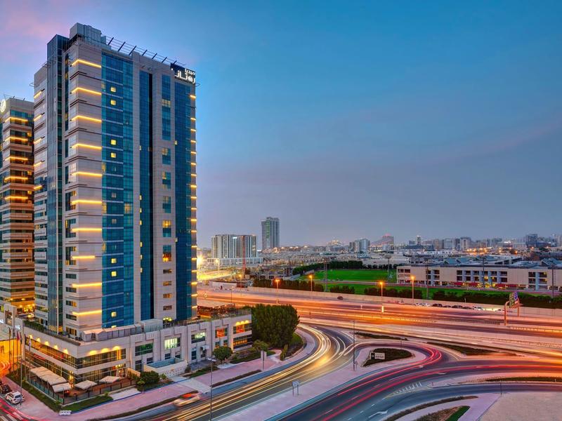 Modern skyscraper next to winding road with light trails at dusk