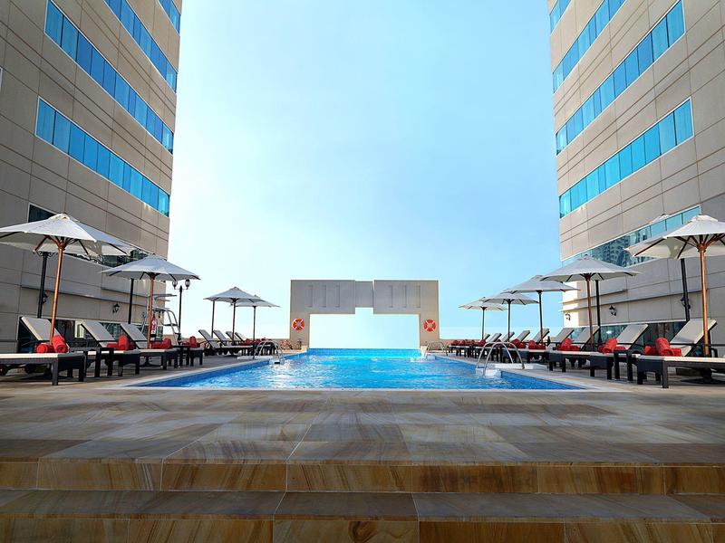 Modern pool between two hotel towers with a view of the sea in the background.