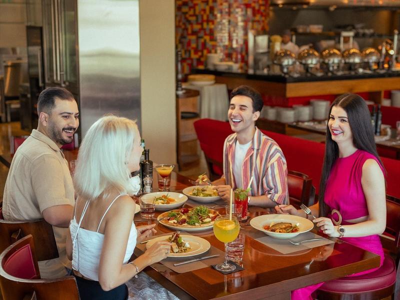 Four people sit at a restaurant table enjoying drinks and meals.