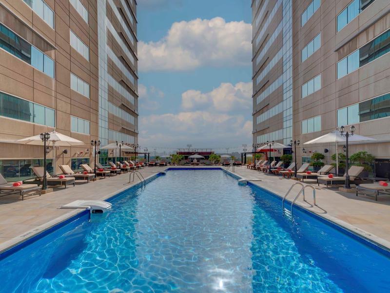 Modern outdoor pool between two high-rise buildings with lounge chairs and umbrellas.