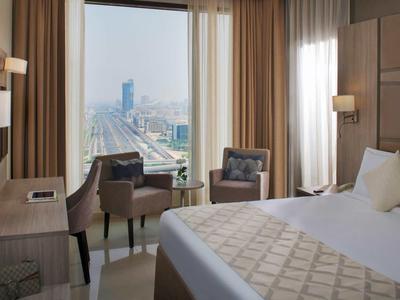 Habitación de hotel moderna con cama grande, escritorio y vista a la ciudad a través de una gran ventana.