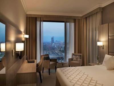 Habitación de hotel moderna con ventana grande y vista a la ciudad al anochecer.