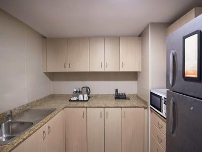 Cocineta pequeña con armarios de madera, microondas y refrigerador en una habitación de hotel.