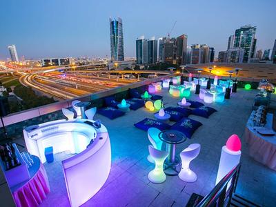 Terraza en la azotea con muebles modernos iluminados en colores y vista de la ciudad al anochecer.