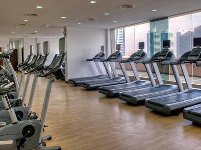 Modern gym with treadmills and stationary bikes by large windows overlooking the city.