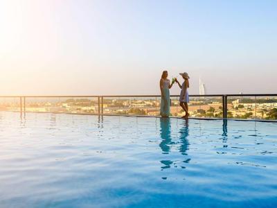 Two women enjoy the view at the infinity pool with cityscape during sunset.