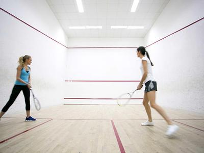 Two women playing squash in a bright squash court with a wooden floor.