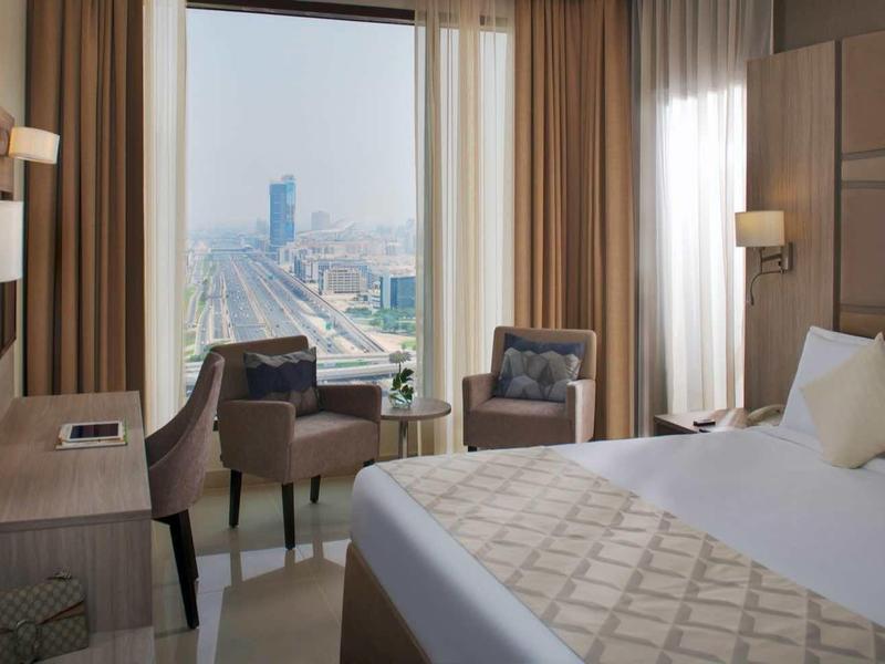 Habitación de hotel moderna con cama grande, escritorio y vista a la ciudad a través de una gran ventana.