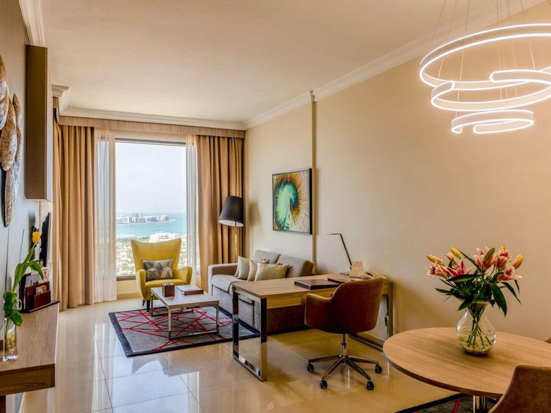 Sala de estar moderna con sofá, escritorio y ventanas panorámicas con vista al exterior.