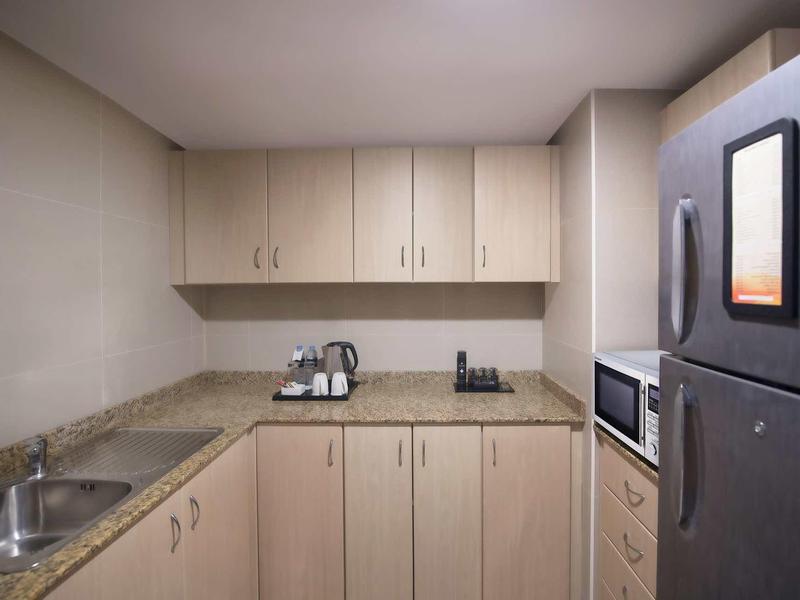 Cocineta pequeña con armarios de madera, microondas y refrigerador en una habitación de hotel.