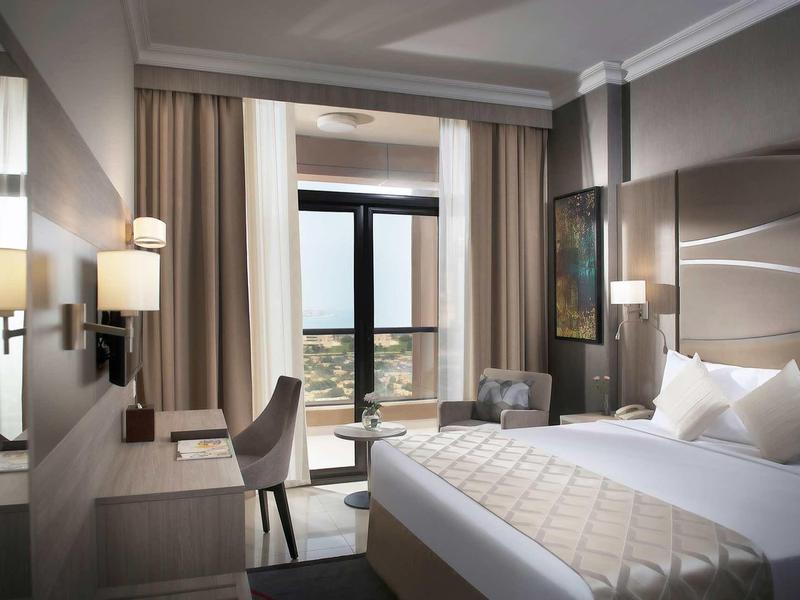 Habitación de hotel moderna con cama doble, escritorio, silla y balcón con vista exterior.